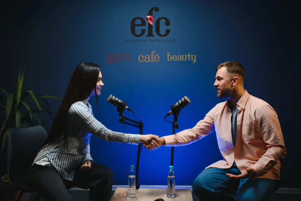 Two people recording a podcast-style conversation in a studio, shaking hands across microphones, representing a professional setting where creators collaborate and learn how to become an influencer.