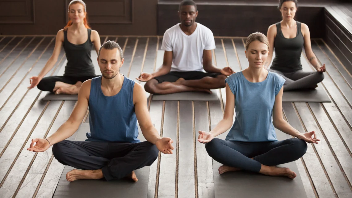 Group of people practicing meditation during yoga classes, sitting cross-legged in a calm studio with peaceful focused expressions.